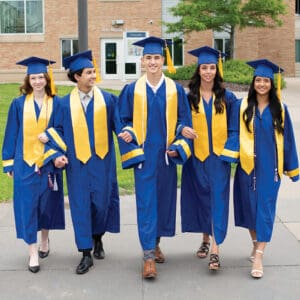 Five graduates in blue gowns and yellow stoles walk together happily.