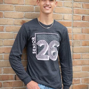 Young man smiling, wearing a black graphic long-sleeve shirt with number 26.